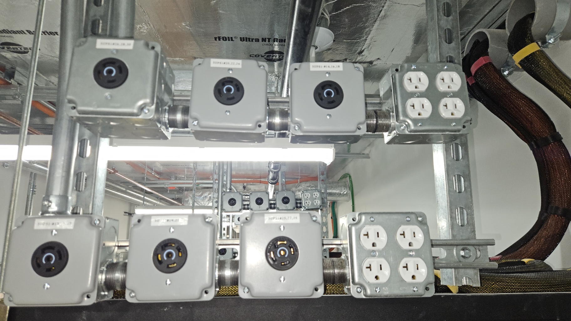 Overhead UPS Twist-Lock Distribution — NEMA L5/L6 twist-lock receptacles and 20A quad outlets on strut, fed by labeled UPS whips for mission-critical loads.