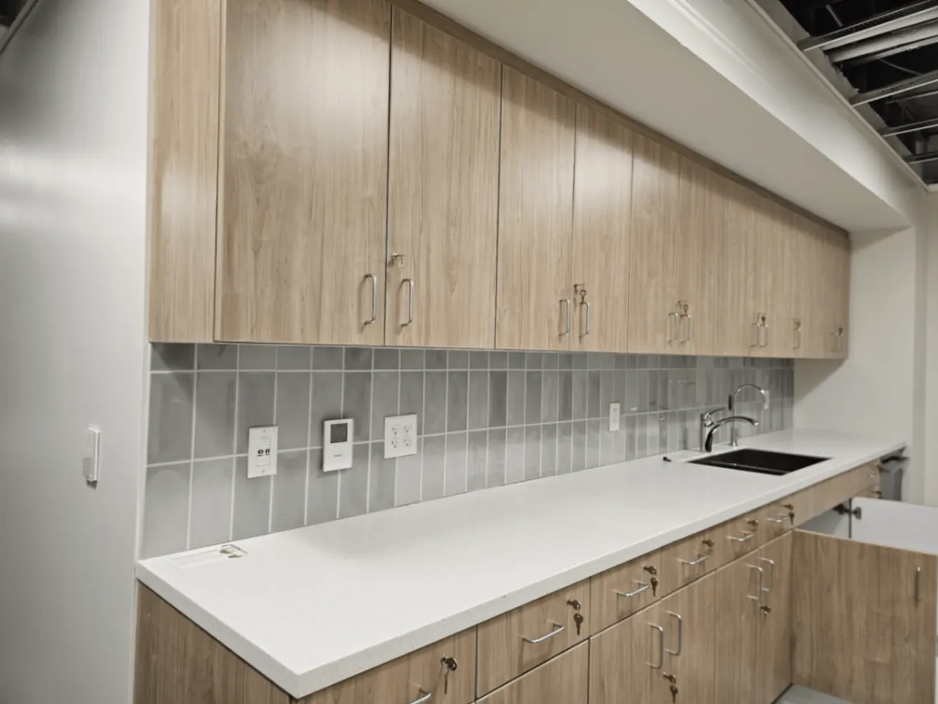 Office Break Room Power & Devices — Quartz-counter break room with thermostat, outlets, and undersink power neatly trimmed in.
