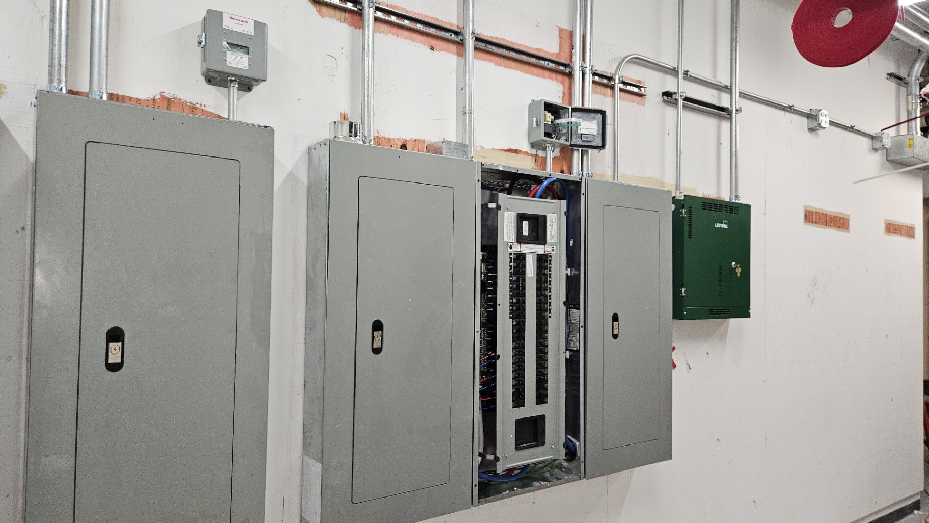 Commercial Panel Bank & Lighting Control Room — Three large panelboards, Honeywell monitoring, and a Leviton GreenMAX relay cabinet — all fed with surface EMT raceway.
